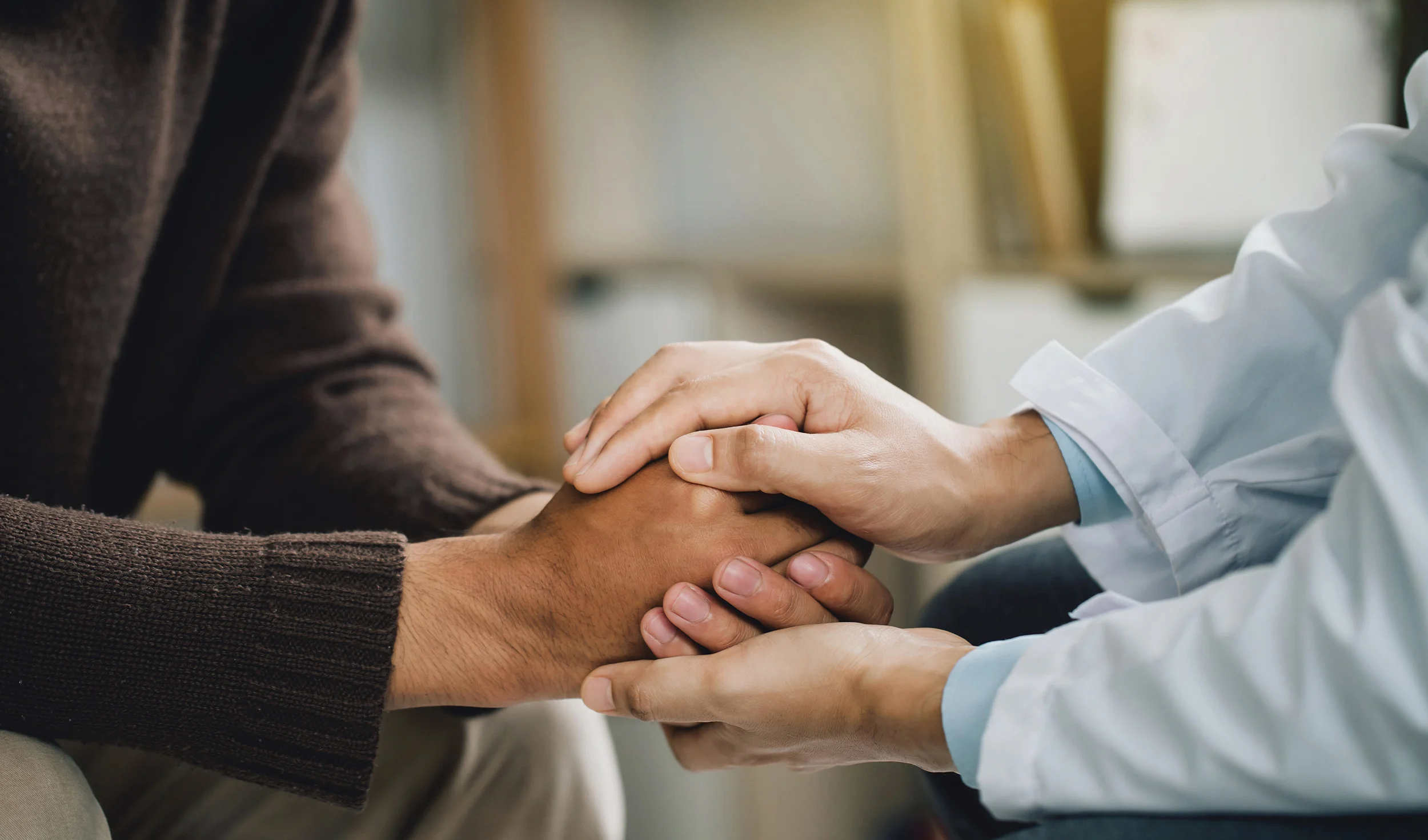 Closeup image of a physician and patient holding hands